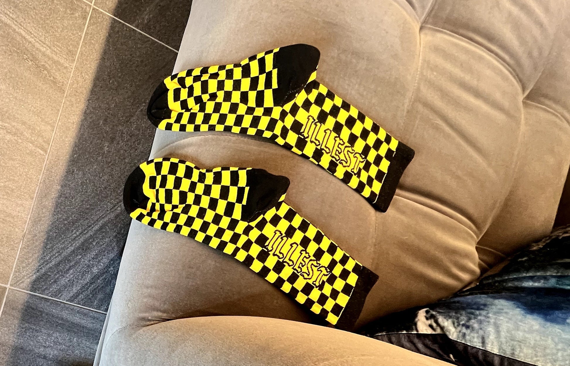 Two pairs of shoes and three socks in our black and yellow checkered style on a couch and white Hoka sneakers on the floor.